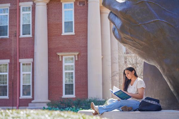 Student reading under hands sculpture